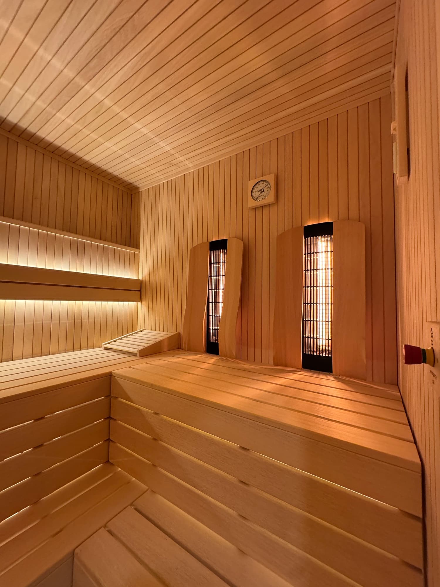 Interior of a wooden Sauna with benches, infrared heater panels, a wall-mounted clock, and warm lighting.