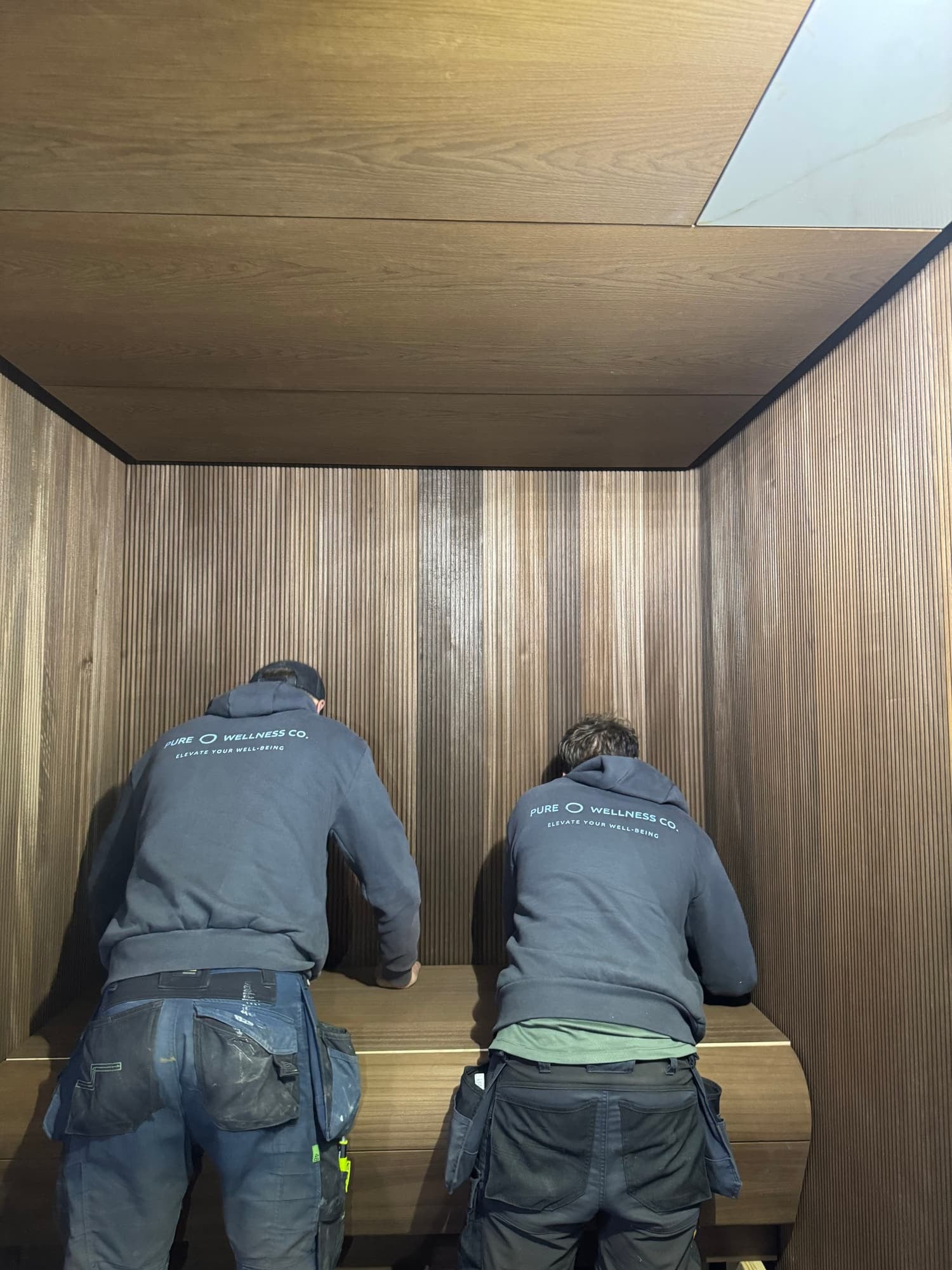 Pure Wellness installers fitting a timber Sauna bench on site